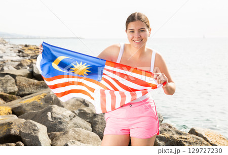 Young woman on coast posing with flag of Malaysia Young woman on coast posing with flag of Malaysia 129727230