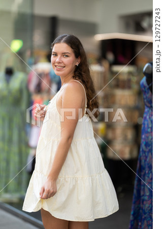 Young girl in white dress is looking for something at street market - looking at goods with interest Young girl in white dress is looking for something at street market - looking at goods with interest 129727243