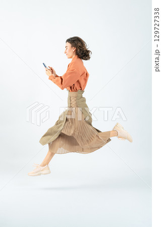 スマホを使いながらジャンプする白人女性の全身写真 129727338