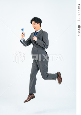 スマホを見ながらジャンプする男性ビジネスパーソンの全身写真 スマホを見ながらジャンプする男性ビジネスパーソンの全身写真 129727363