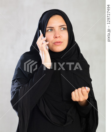Young woman dressed in traditional islamic clothes looking up something on her phone 129727494