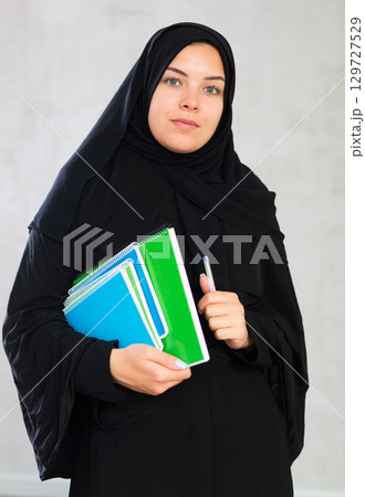 Young student woman dressed in traditional islamic clothes holding notebooks 129727529