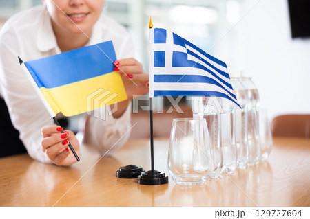 Young woman puts flags of Ukraine and Greece on table in office Young woman puts flags of Ukraine and Greece on table in office 129727604
