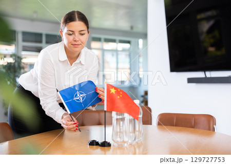 Young lady sets miniatures flags of Chinа and NATO before international negotiations 129727753