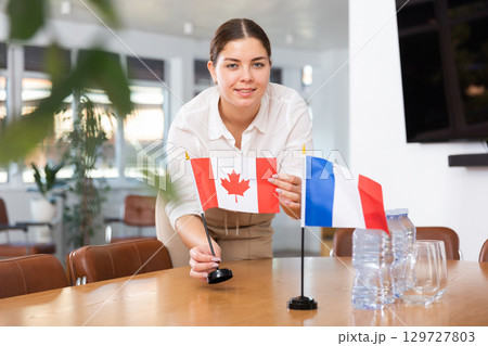 Employee of delegation prepares negotiating table - sets up flag of Canada and France 129727803