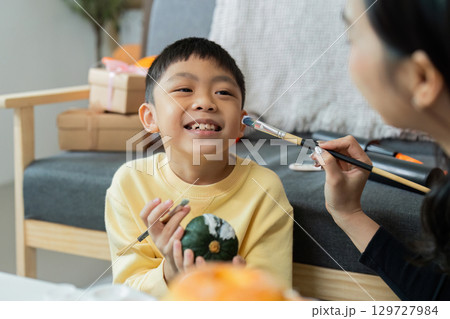 Halloween Crafting. Child enjoying pumpkin painting with mother s guidance. 129727984