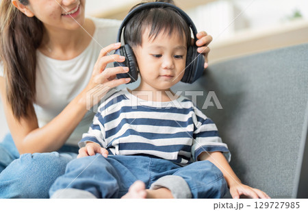 Mother and child enjoying music together with headphones at home 129727985