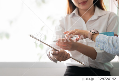 Collaboration. Two women discussing project details with a tablet in a bright office. Collaboration. Two women discussing project details with a tablet in a bright office. 129728142