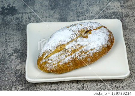 A small, freshly baked loaf of bread dusted with powdered sugar, sitting on a white rectangular plate. 129729234