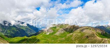 Breathtaking Mountain Vista Panorama of Alpine Peaks and Lush Meadows Under a Cloudy Sky Breathtaking Mountain Vista Panorama of Alpine Peaks and Lush Meadows Under a Cloudy Sky 129729334