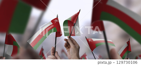 Oman flags in their hands on a blurred urban background 129730106