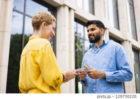Two people exchanging money outdoors near a building. The man is holding cash, the woman is receiving it. 129730220