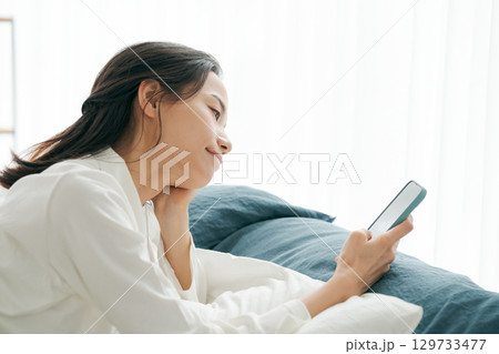寝ながらスマホを見るパジャマの女性 129733477