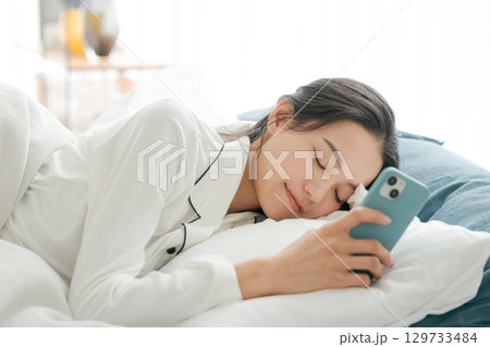 寝ながらスマホを見るパジャマの女性 129733484