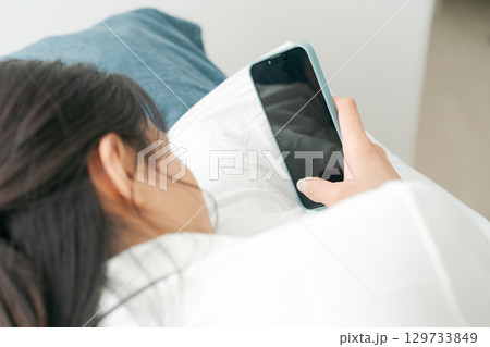 ベッドでスマートフォンを使う若い女性 129733849