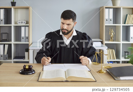 Portrait of male judge wearing judicial robe working in office having court verdict. Portrait of male judge wearing judicial robe working in office having court verdict. 129734505