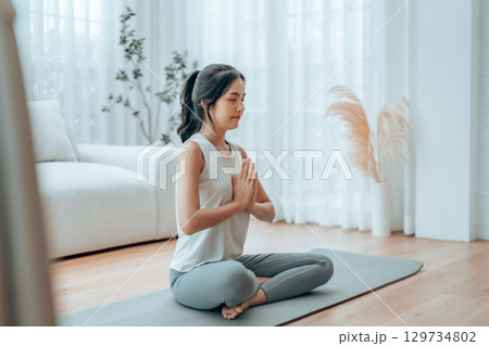 Young Asian woman meditating in lotus position at home 129734802