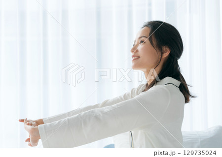 朝起きて窓を開けるパジャマの女性 129735024