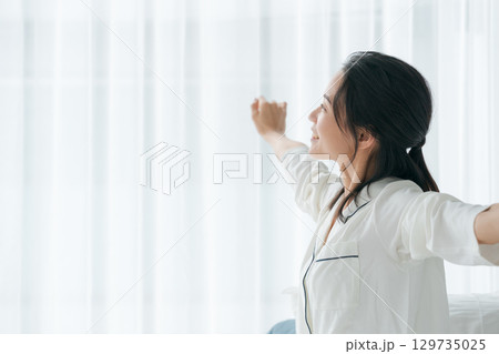 朝起きて窓を開けるパジャマの女性 129735025