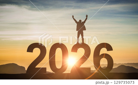 Silhouette of a successful person standing on 2026 number, celebrating with arms raised at sunrise, a concept of achievement 129735073