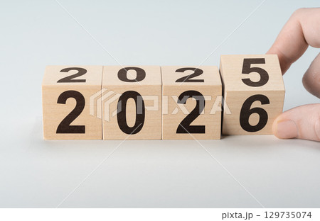 Male hand turning wooden cube to reveal year 2026, leaving 2025 behind. New beginnings and fresh start business concept 129735074