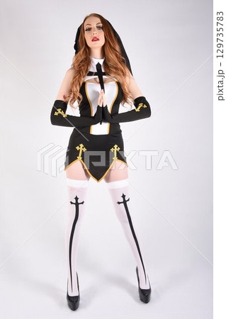 Tall, attractive, redhead model dressed as a fantasy Nun, isolated against a white background 129735783