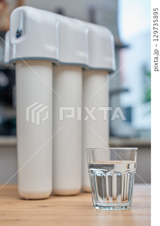 Glass of filtered drinking water and water filtration system on kitchen table Glass of filtered drinking water and water filtration system on kitchen table 129735895