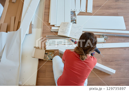 Woman assembling furniture with tools and instruction manual at home 129735897
