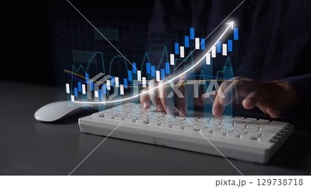 Hands Typing on Keyboard with Stock Market Data Visualization in Background Showing Increasing Financial Growth and Trends in Dark Environment Copula 129738718