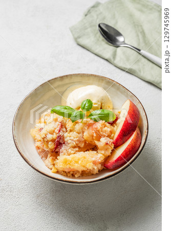 Peach crumble or cobbler with vanilla ice cream scoops and cinnamon on a plate on a light background Peach crumble or cobbler with vanilla ice cream scoops and cinnamon on a plate on a light background 129745969