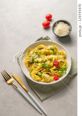 Tortellini pasta with parmesan, pesto and basil in a plate on a light background with tomato Tortellini pasta with parmesan, pesto and basil in a plate on a light background with tomato 129745970