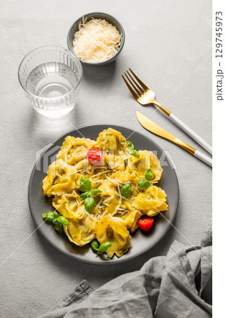 Tortellini pasta with parmesan, pesto and basil in a plate on a light background with glass of water 129745973