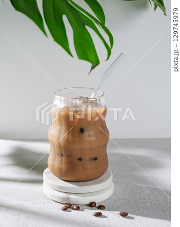 Ice latte coffee in a glass with milk and straw on a light background with coffee beans, monstera Ice latte coffee in a glass with milk and straw on a light background with coffee beans, monstera 129745979