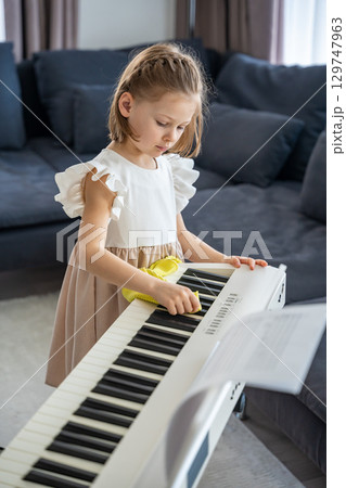 Little girl carefully cleaning her piano at home in the living room. Early childhood education through music includes care, responsibility and respect for the instrument. 129747963