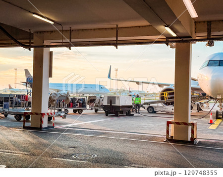 Airport ground crew loading luggage at sunrise. Travel logistics, aviation operations, and early morning airport workflow on the tarmac. 129748355