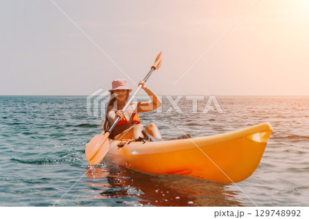 Kayaking Woman Ocean Sunset - Happy woman kayaking on the ocean during a sunset. 129748992