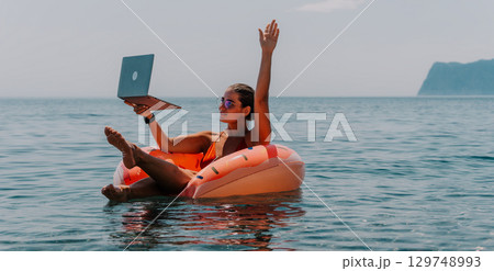 Laptop, Beach, Work - Woman on inflatable ring working on her laptop in the ocean. 129748993