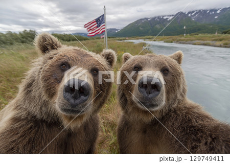 Two adult bears take a selfie on a phone camera against the backdrop of nature and the US flag. 129749411