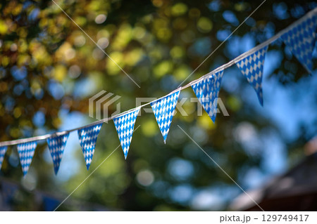 Oktoberfest decoration. Blue and white triangular flags in the form of a garland between the trees. 129749417