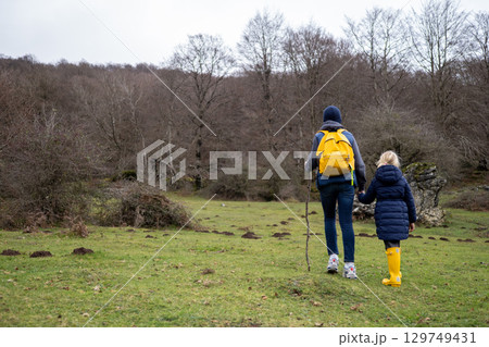 Father, daughter hiking woodland trail, yellow boots matching backpacks, winter landscape surrounding them 129749431