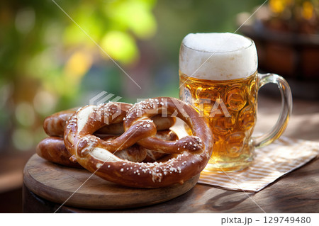 German pretzel and a glass of beer and sausages on wooden desk on blurred street background. Oktoberfest celebration. 129749480