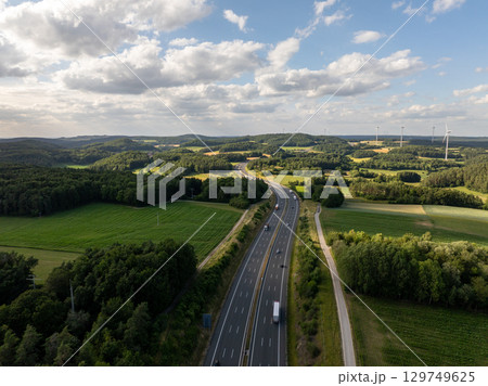 Aerial view of highway a9 crossing the Bavarian countryside near pegnitz, with trucks driving on asphalt road, green fields, forests and wind turbines in background Aerial view of highway a9 crossing the Bavarian countryside near pegnitz, with trucks driving on asphalt road, green fields, forests and wind turbines in background 129749625