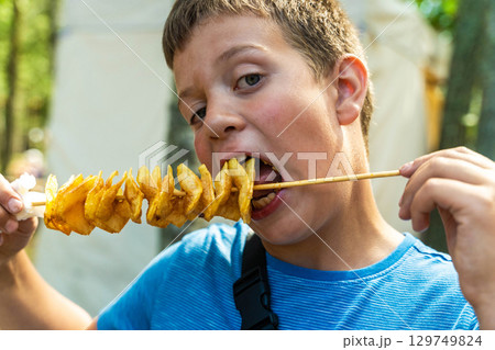 Boy eating tornado potato on a stick at street food festival Boy eating tornado potato on a stick at street food festival 129749824