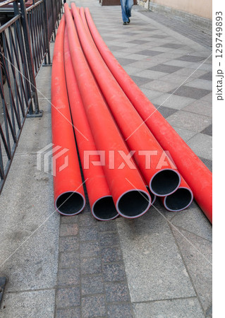 Red plastic pipes lying on the sidewalk during roadworks 129749893