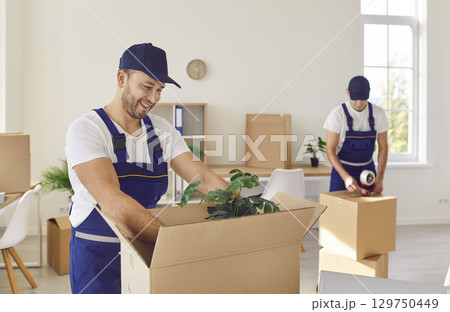 Professional workers of moving service packing cardboard boxes. Moving day concept. Professional workers of moving service packing cardboard boxes. Moving day concept. 129750449