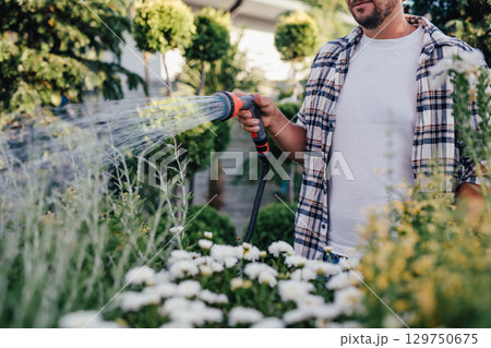 Close up of garden center worker watering plants with hose in greenhouse. 129750675