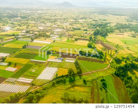 Aerial view of agricultural landscape with greenhouses and cultivated fields. Rural infrastructure, sustainable farming, and seasonal land use in summer countryside. 129751454