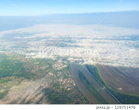 Aerial view of city, river, and cloud layer from above. Urban sprawl, natural border, and weather conditions over landscape in morning light. 129751476