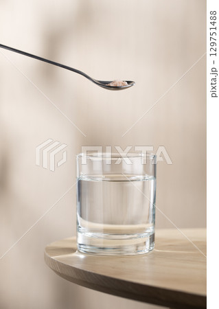A spoon of Himalayan salt is being added to a glass of drinking water. 129751488