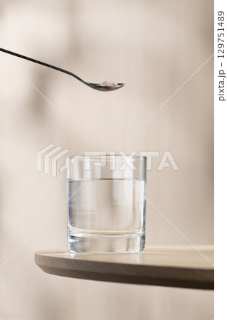A spoon of Himalayan salt is being added to a glass of drinking water. 129751489